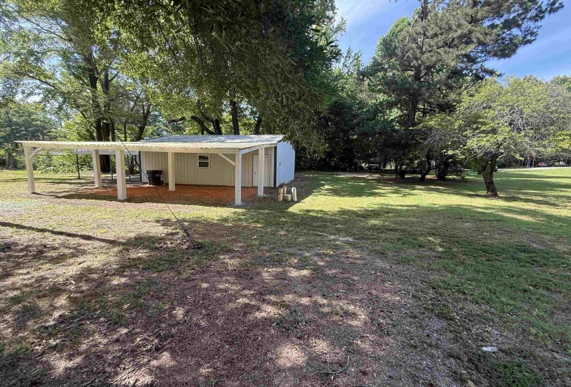 Detached outbuilding featuring a white paneled exterior, covered patio area with exposed rafters, and a side entry door