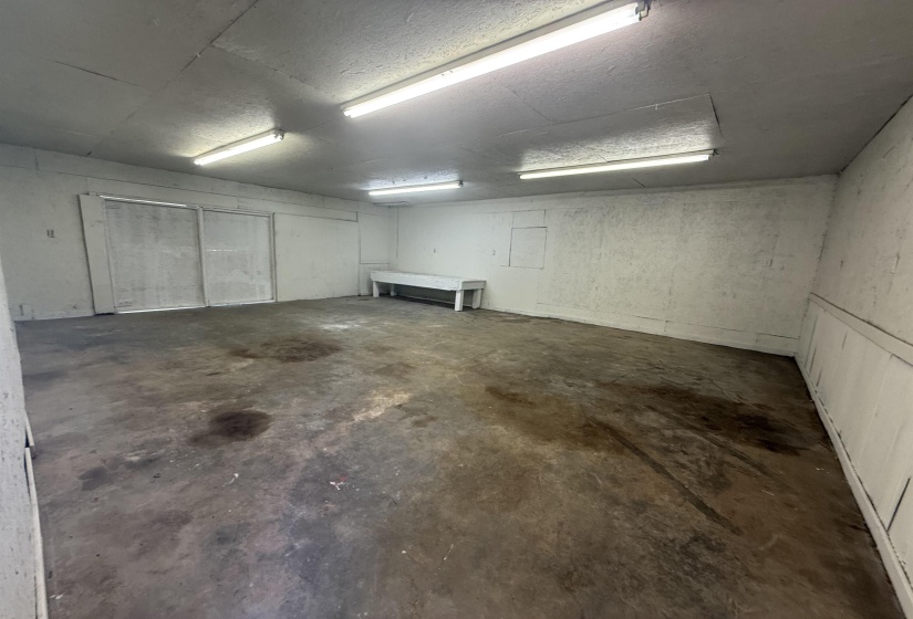 Spacious interior room with concrete flooring, fluorescent lighting, and white walls