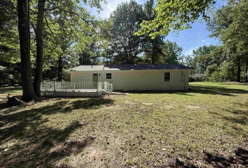 Rear exterior featuring a white painted wood deck with lattice skirting and a privacy railing, set against a backdrop of mature trees