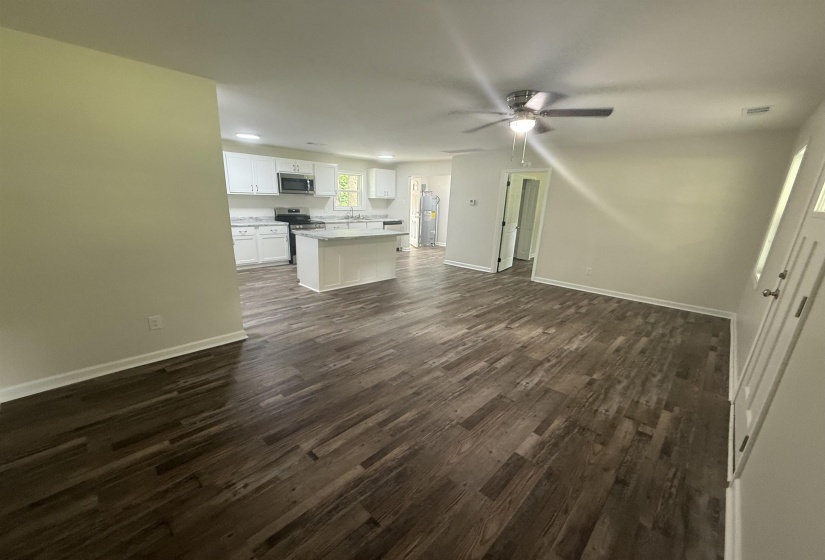 Open-concept living area featuring wood-finish flooring, a ceiling fan with light, and white baseboards