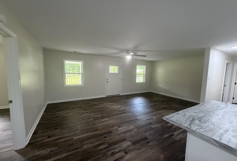Spacious living area featuring wood-finish flooring, light-toned walls, and a ceiling fan