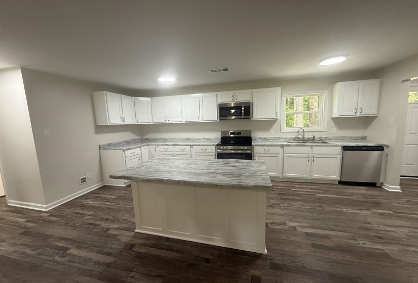 Modern kitchen featuring white cabinetry, a central island with a stone-look countertop, stainless steel appliances, wood-finish flooring, and recessed lighting