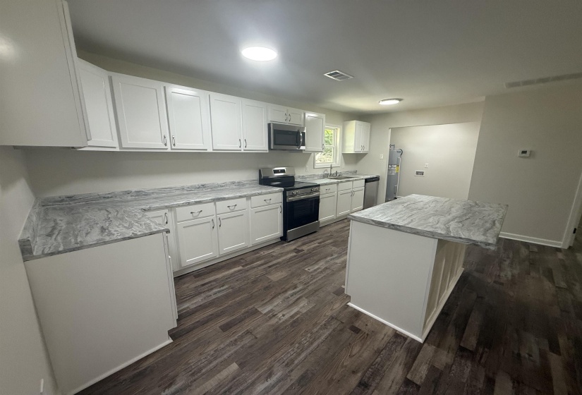 Modern kitchen featuring white shaker cabinetry, wood-finish flooring, a central island with countertop seating, stainless steel appliances, and a double basin sink