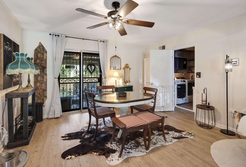 Open-concept living area with wood-finish flooring, a ceiling fan with integrated lighting, and a sliding glass door with wrought iron security gate