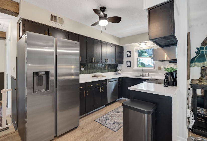 Well-appointed kitchen featuring dark cabinetry with gold-tone hardware, a stainless steel side-by-side refrigerator, and a stainless steel dishwasher
