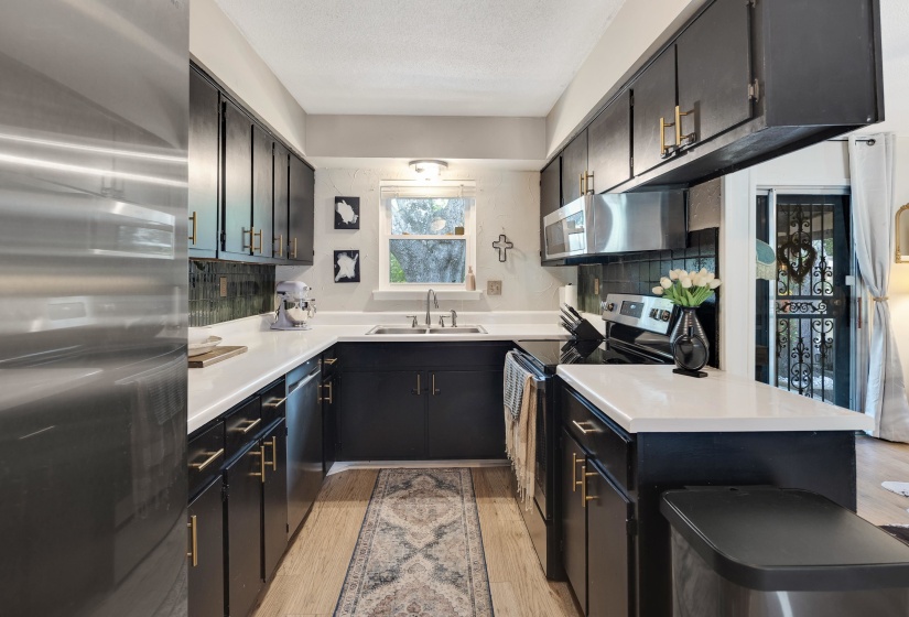 Galley kitchen featuring dark cabinetry with gold-tone hardware, white countertops, and a subway tile backsplash