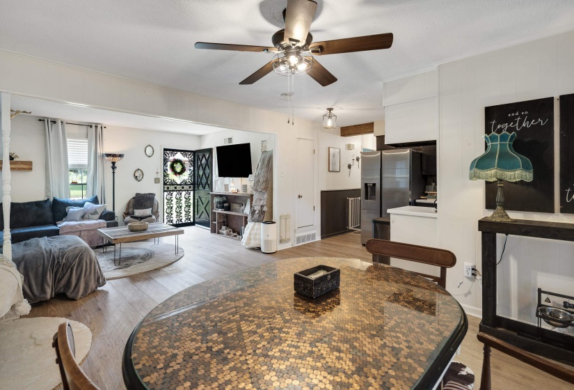 Open-concept living space featuring wood-finish flooring, a ceiling fan with integrated lighting, and a kitchen area with a stainless steel refrigerator