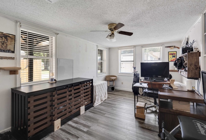 Spacious room featuring wood-finish flooring, multiple windows with blinds, a ceiling fan, and white walls