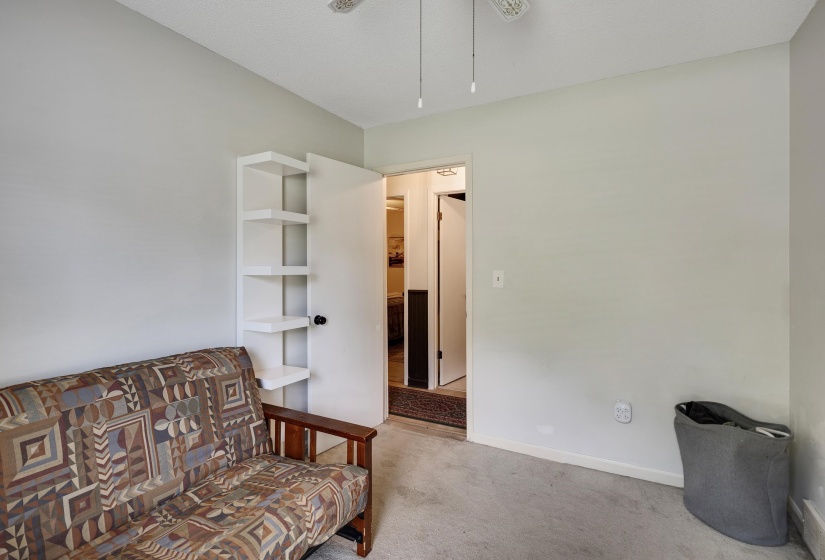 Room featuring light-colored walls, ceiling fan, carpet flooring, a white built-in shelving unit, and a doorway