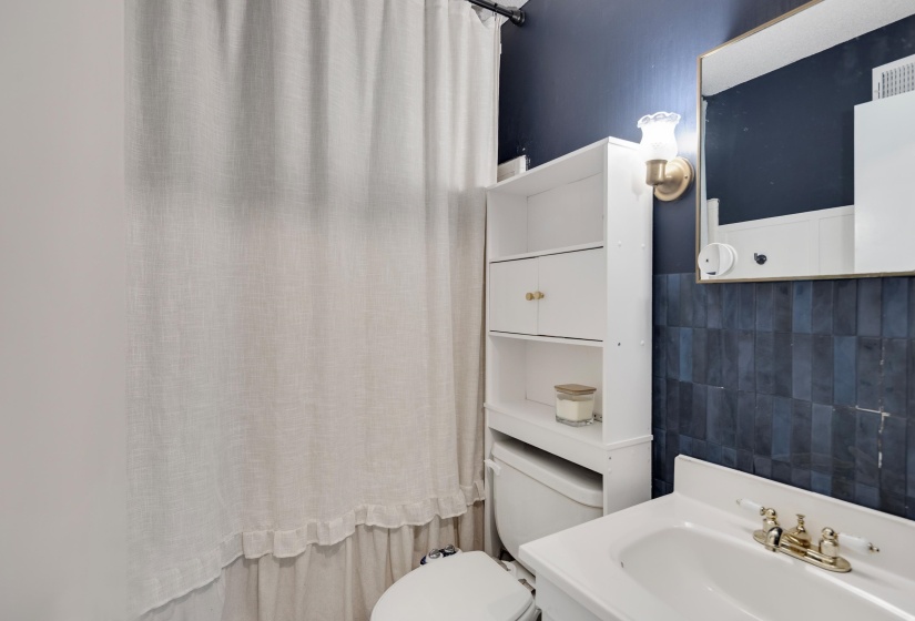 Bathroom featuring a white toilet, built-in shelving, and a vanity with a white sink and brass-finish faucet