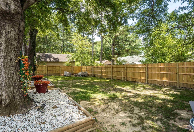Generous backyard space featuring a wood privacy fence, expansive lawn, mature trees, and a decorative white stone bed with log-style border