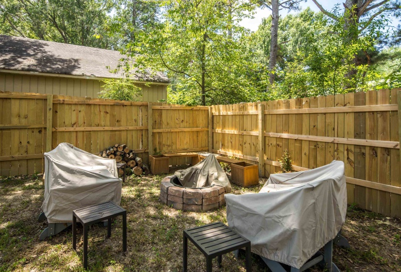 Backyard space featuring a stone-ringed fire pit, wood privacy fence, and mature perimeter trees