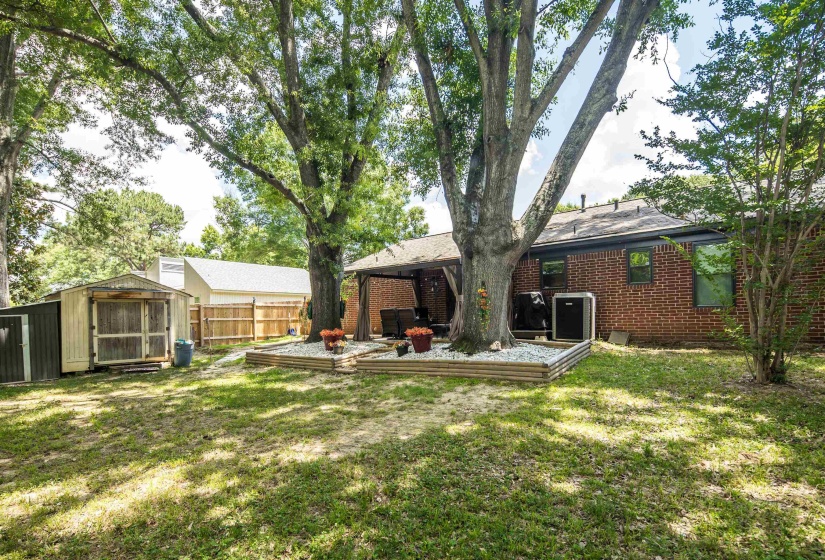 Expansive grass yard with mature trees, a covered patio, and a brick exterior