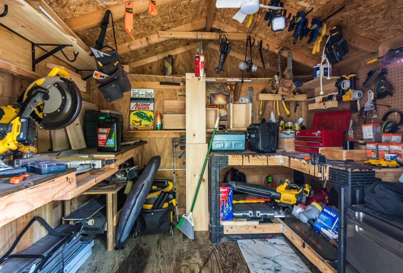 Well-appointed utility shed featuring built-in shelving, organized tool storage, a ceiling fan, and durable wood-finish flooring