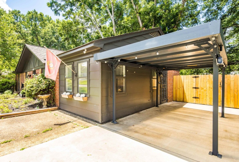 Detached covered carport with string lights, concrete pad, and full wood privacy fencing