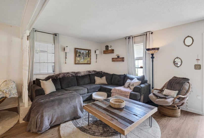 Bright living area featuring wood-finish flooring, white walls, and a large window with blinds