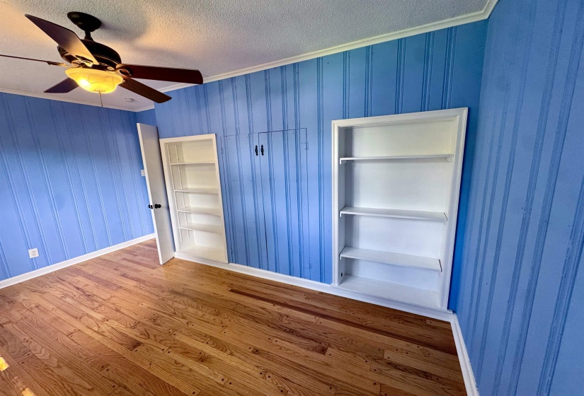 Room featuring wood-finish flooring, blue vertical paneling, and white crown molding
