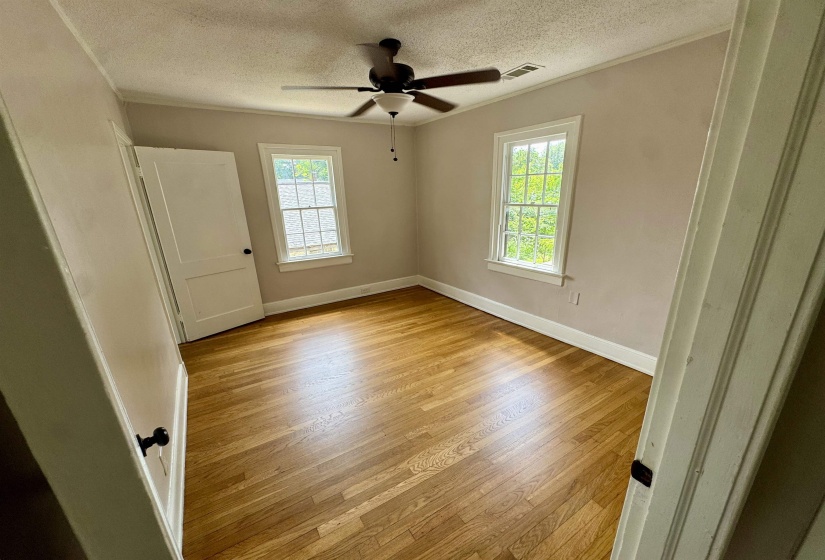 Room featuring wood-finish flooring, two large windows, a ceiling fan with integrated lighting, and a white paneled door