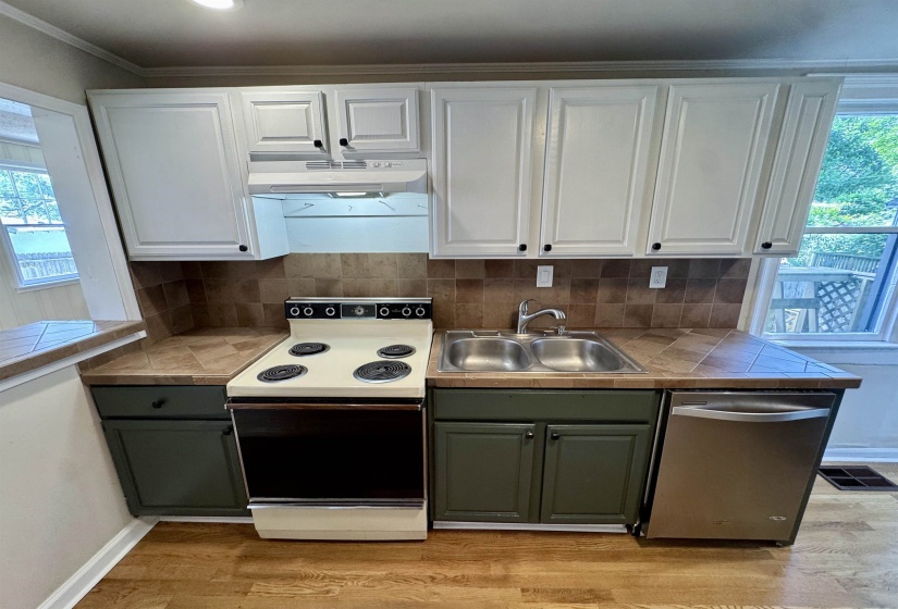Kitchen featuring white upper cabinetry, forest green lower cabinetry, a tile backsplash, and wood-finish flooring