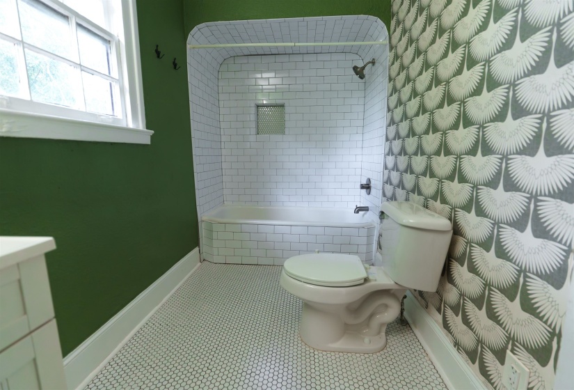 Bathroom featuring white hex tile flooring, a white subway-tiled tub/shower combination with a built-in niche, and a patterned wallpaper accent wall