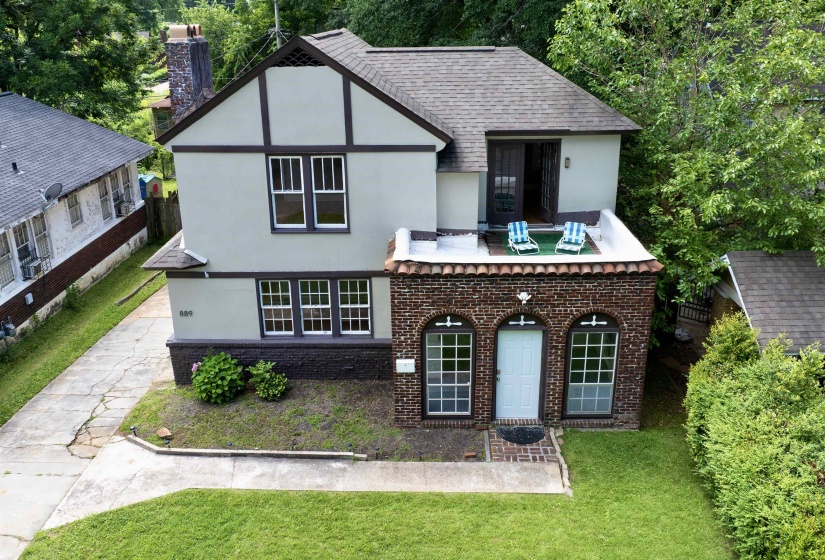 Tudor-style exterior with a stucco and timber frame upper level, a brick lower level, a front-facing balcony, an arched entry door, and multi-pane windows