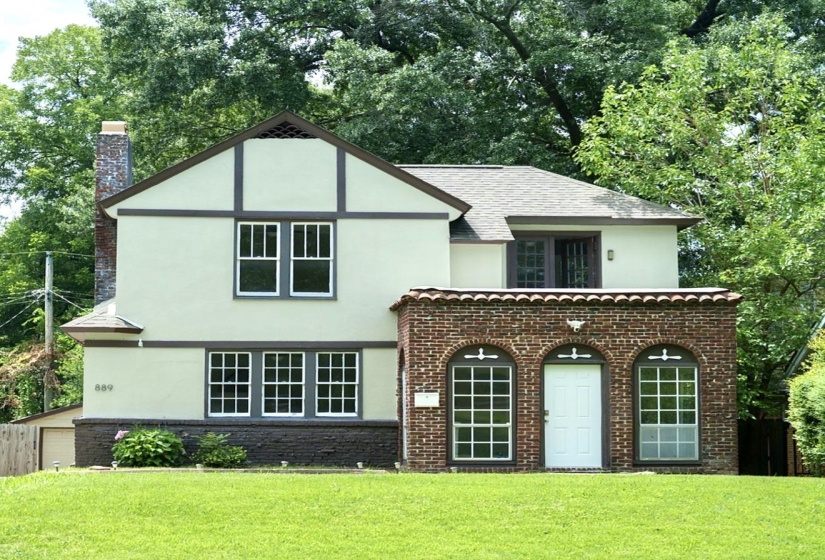 Tudor Revival architecture featuring stucco and half-timbering, brick lower facade, arched windows, a white entry door, and a shingled roof