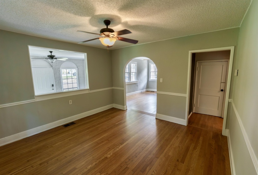 Spacious room featuring wood-finish flooring, a ceiling fan with integrated lighting, and a decorative chair rail molding