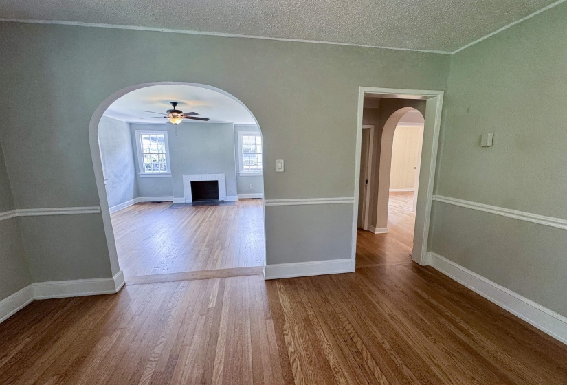 Hardwood flooring extends throughout the space, featuring arched doorways, a ceiling fan, and a fireplace with a white mantel and black firebox