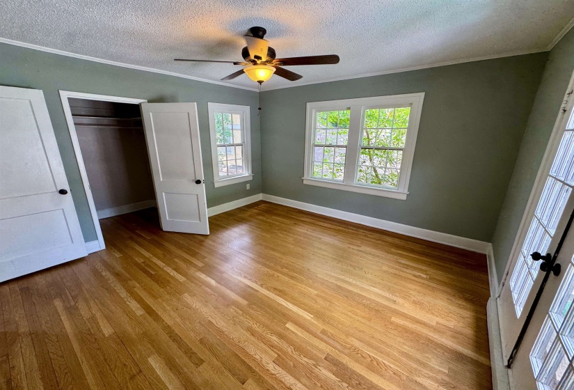 Bright room featuring wood-finish flooring, two large windows, a ceiling fan with integrated lighting, and a closet with bifold doors