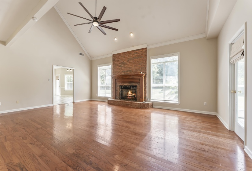 Spacious room featuring vaulted ceilings, wood-finish flooring, and a brick fireplace with a wood mantel