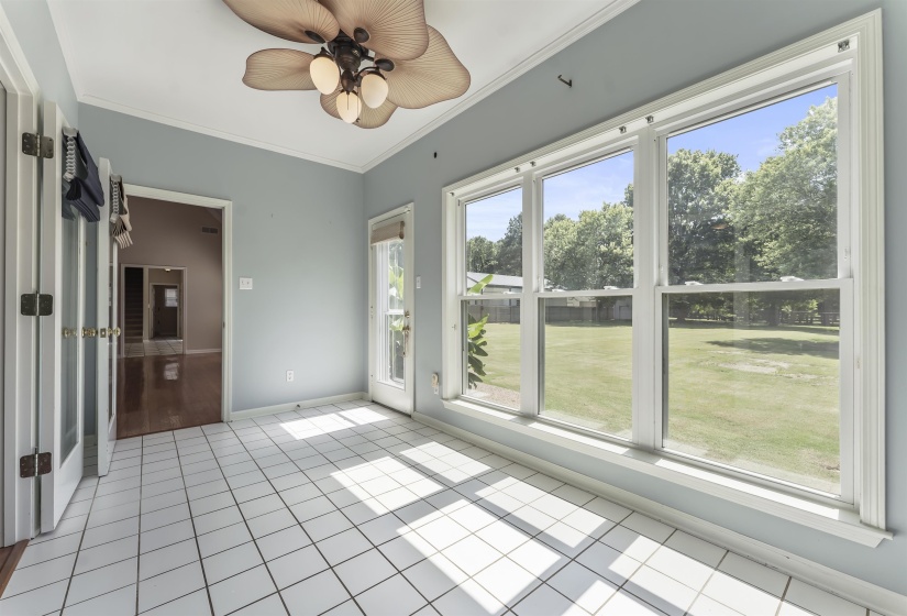 Spacious room featuring large windows, a full-light exterior door, white square tile flooring, and a ceiling fan with light fixture