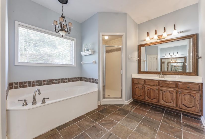 Primary bath featuring a soaking tub with decorative tile surround, separate shower enclosure, and a large vanity with wood cabinetry and a framed mirror