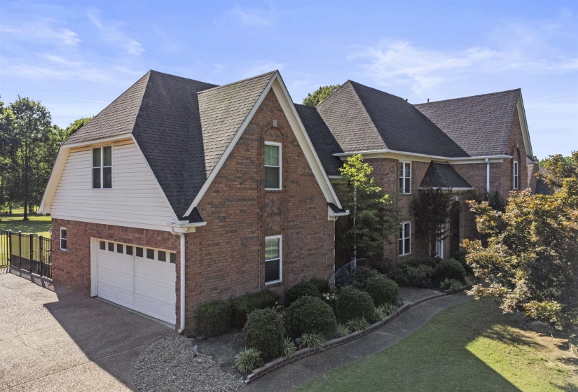 Brick exterior with gabled roof lines, attached two-car garage, upper-level dormer, paved driveway, and mature landscaping