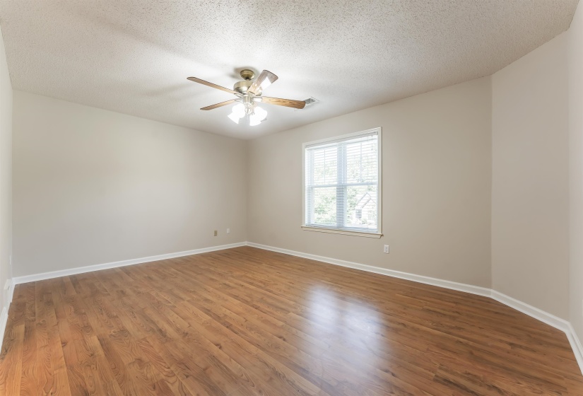 Spacious room featuring wood-finish flooring, neutral-toned walls, and a window with blinds
