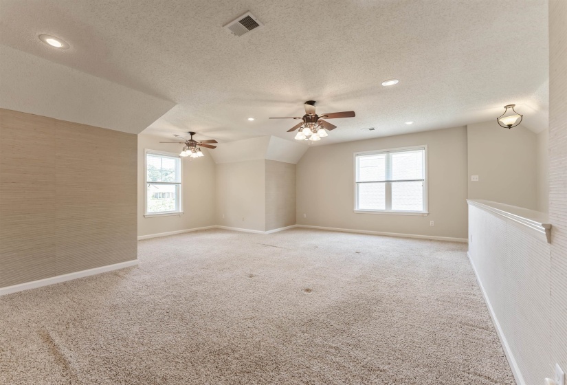 Spacious carpeted room featuring vaulted ceilings, multiple windows, recessed lighting, and two ceiling fans