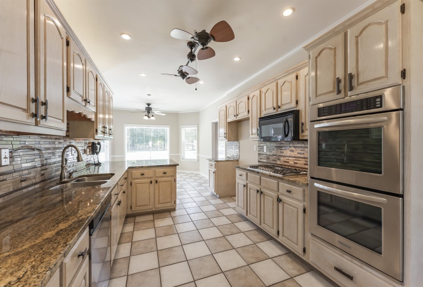 Spacious kitchen featuring light wood cabinetry, granite countertops, stainless steel double ovens, a gas cooktop, and a tile backsplash