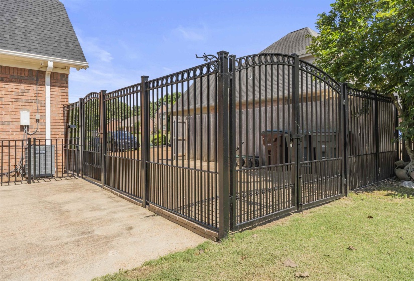 Custom black wrought iron fencing with an arched gate, brick perimeter, and a concrete patio space
