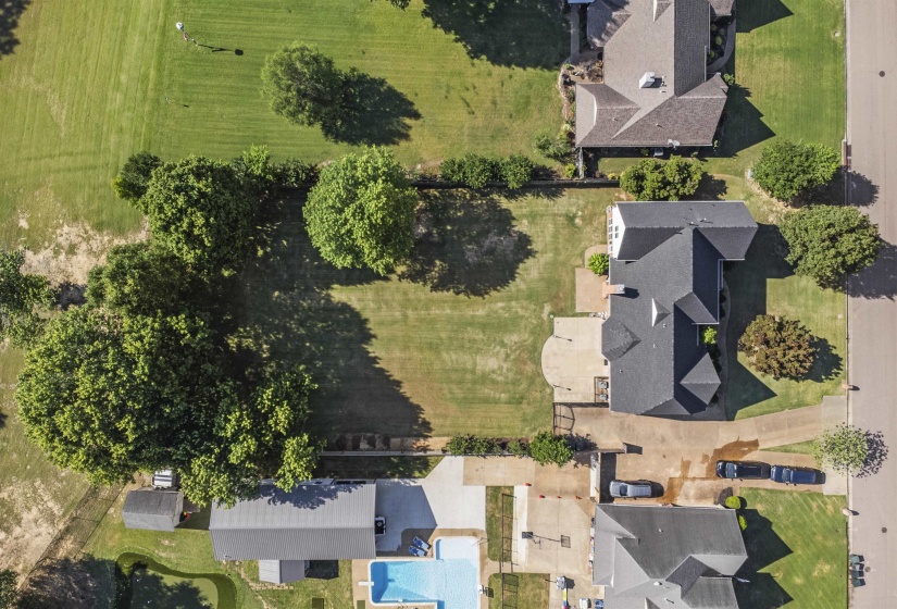 Expansive property featuring a dark-shingled roofline, concrete drive, and mature trees providing natural shade