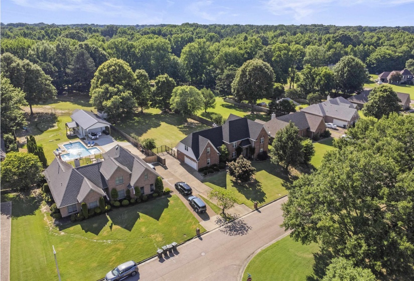 Brick residence featuring a private swimming pool, expansive green lawn, and mature trees