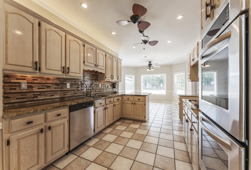 Kitchen featuring light-toned cabinetry, stainless steel appliances, a multi-tone tile backsplash, and checkerboard floor tiling