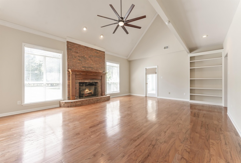 Spacious living area featuring high vaulted ceilings, wood-finish flooring, a brick fireplace with a wood mantle, and an integrated ceiling fan