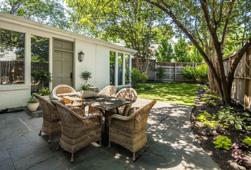 Expansive stone patio with direct access to the interior, complemented by a manicured lawn and mature perimeter trees