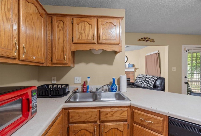 Kitchen featuring wood cabinetry, a double basin stainless steel sink, light-toned countertops, and black built-in appliances