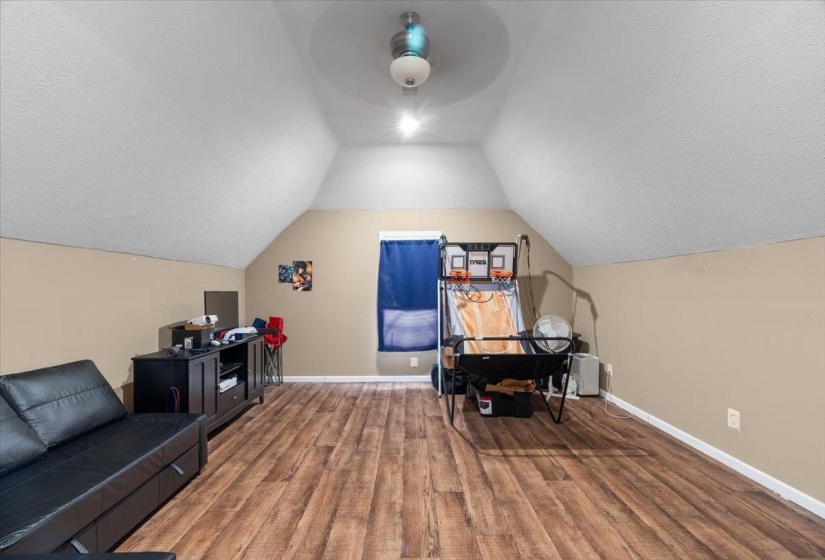 Spacious loft area featuring wood-finish flooring, a vaulted ceiling, and neutral wall tones