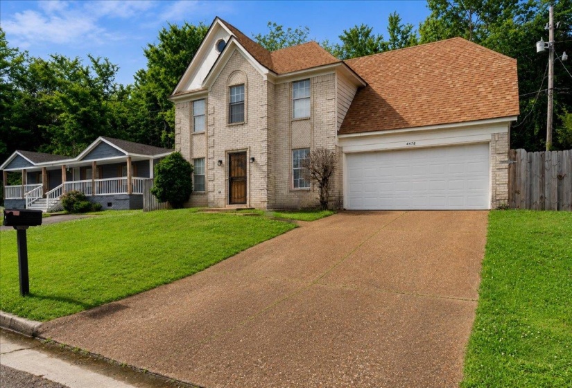 Two-story brick exterior featuring a multi-gabled roofline, an attached two-car garage, an elongated driveway, and a front lawn with established landscaping