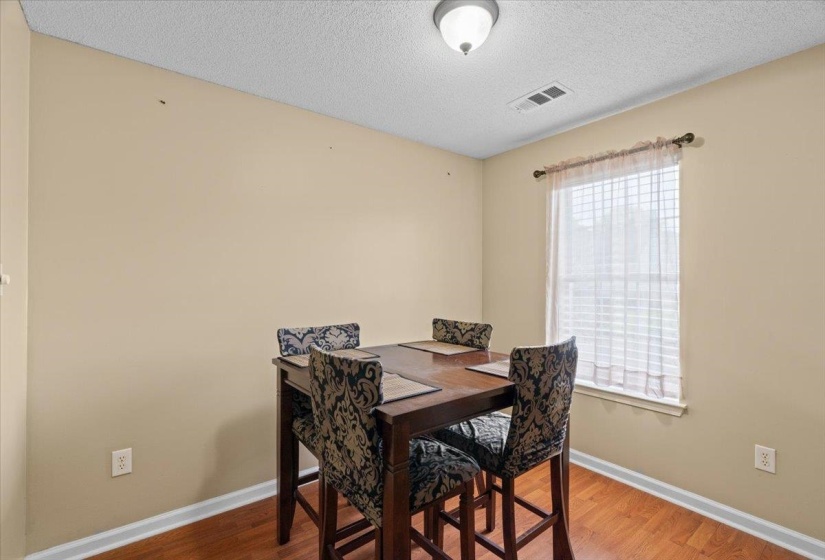 Warm-toned walls and wood-finish flooring define this bright room, featuring a window with blinds and sheer curtains