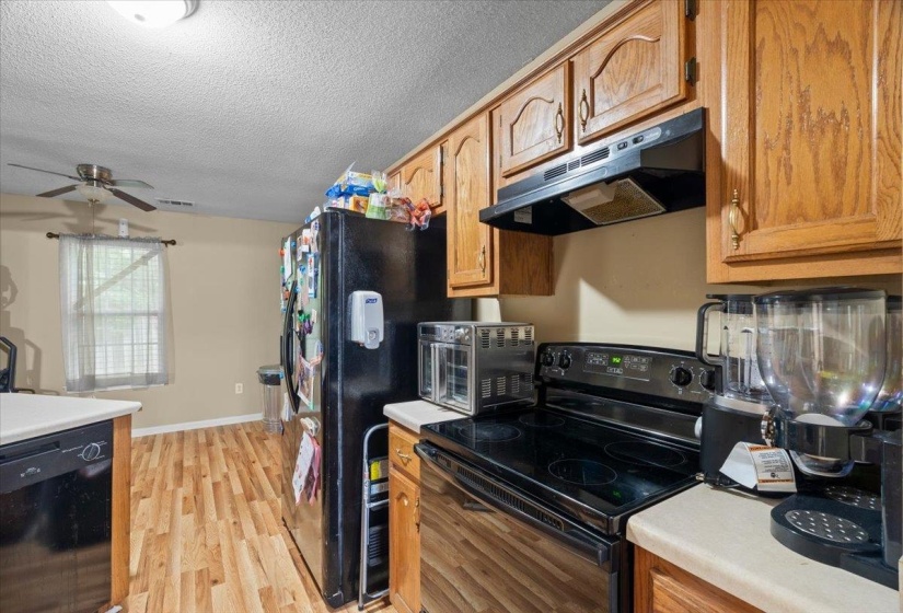 Kitchen featuring wood-finish flooring, a black range with an overhead hood, wood cabinetry, and a ceiling fan in the adjoining space