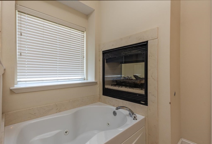 Built-in jetted tub featuring a deck-mounted chrome faucet, stone surround, and an integrated fireplace with a stone hearth