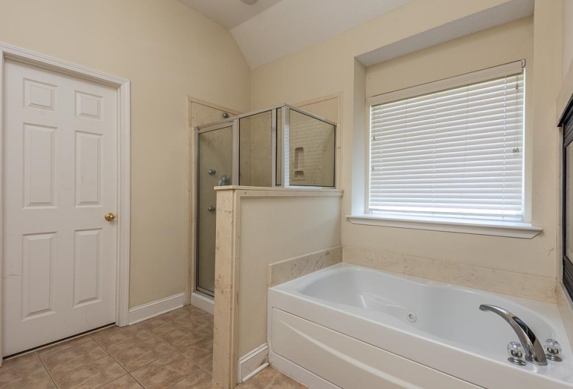 Soaking tub with chrome fixtures, an adjacent glass-enclosed shower, and a large window with blinds