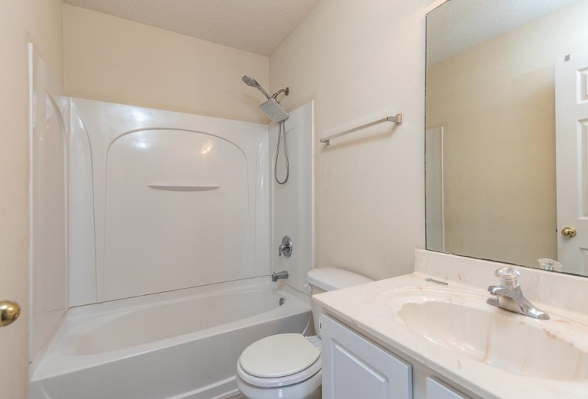 Full bathroom featuring a white tub and shower combination with a rainfall showerhead, a toilet, and a vanity with an integrated sink and mirror